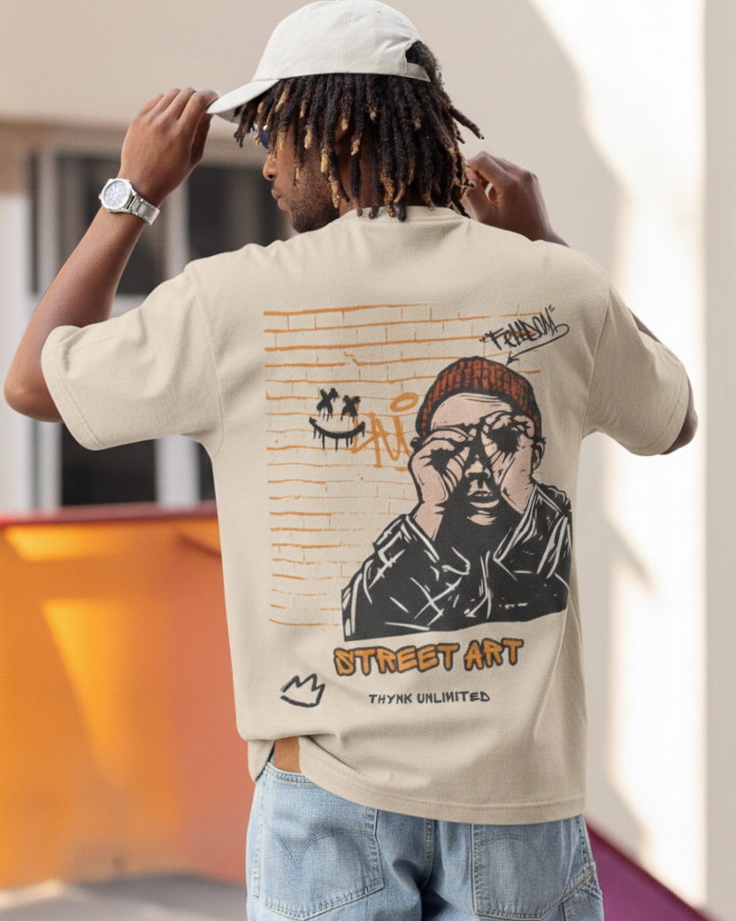 Person wearing a beige t-shirt with street art design, standing outdoors.